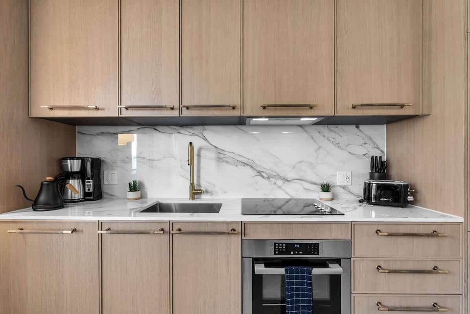 Sleek kitchenette with marble backsplash, brass fixtures, and modern appliances. Coffee maker, toaster, cooktop, and oven—fully equipped for your Miami stay.