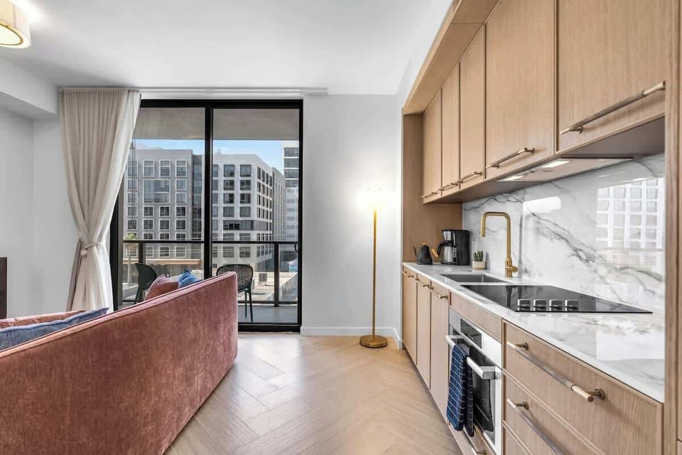 Modern kitchenette with marble backsplash and full appliances, opening to a bright living area with balcony access and Wynwood views. Cook, relax, and enjoy Miami in style.