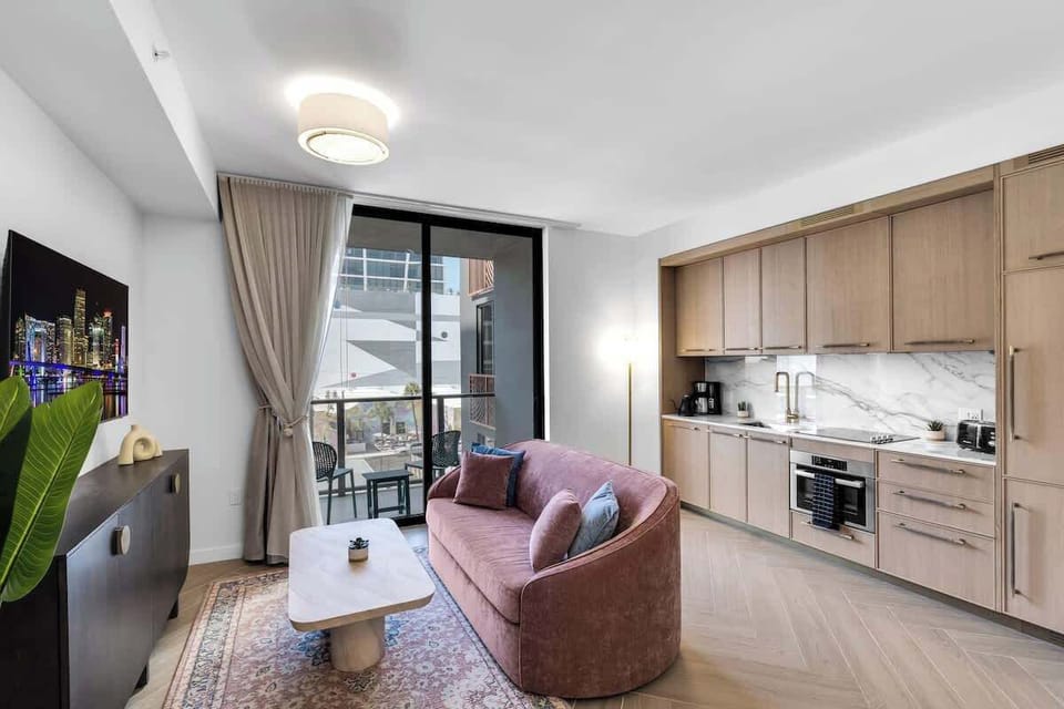 Open-concept living at its finest! Sleek kitchenette, cozy pink sofa, and balcony access with Miami views—everything you need for the perfect Wynwood stay.