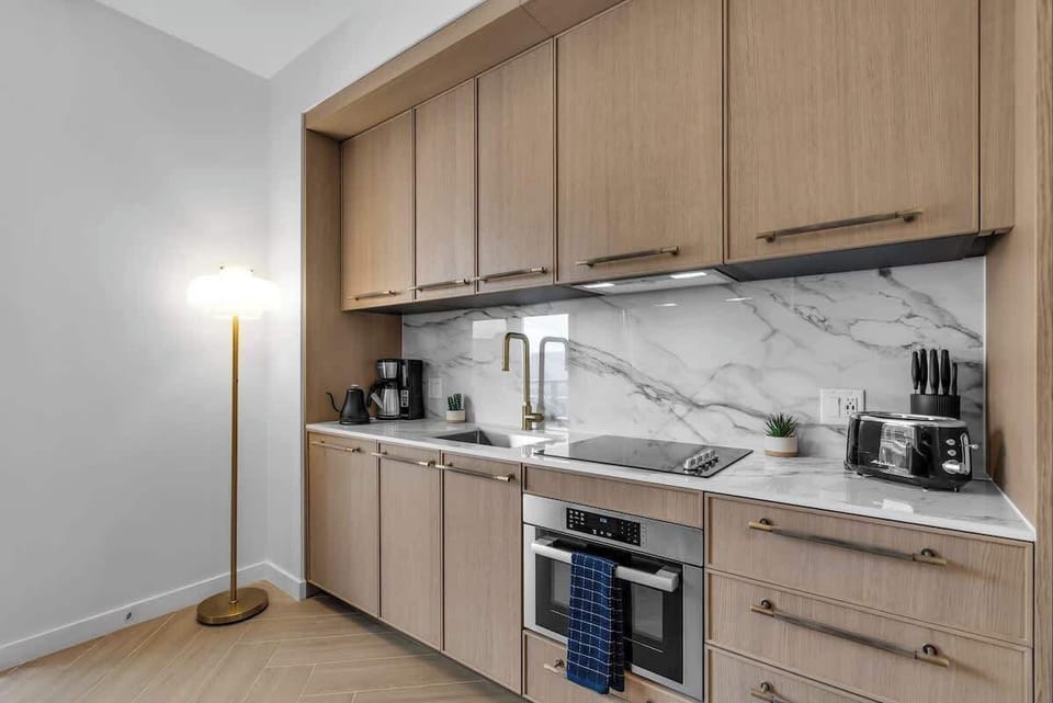 Fully equipped kitchenette with marble backsplash, modern wood cabinetry, and all the essentials—coffee maker, toaster, cooktop, and oven. Cook up a storm during your Miami stay!