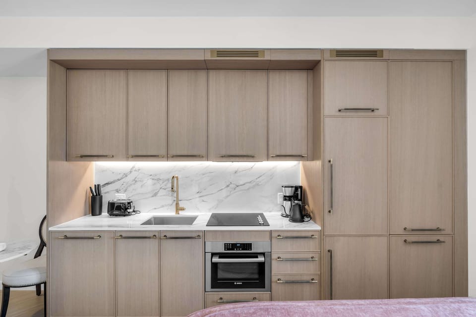 Whip up your favorite meals in the sleek kitchenette featuring marble backsplash, modern appliances, and ample storage. Coffee maker, toaster, cooktop, and oven—everything you need to feel right at home.