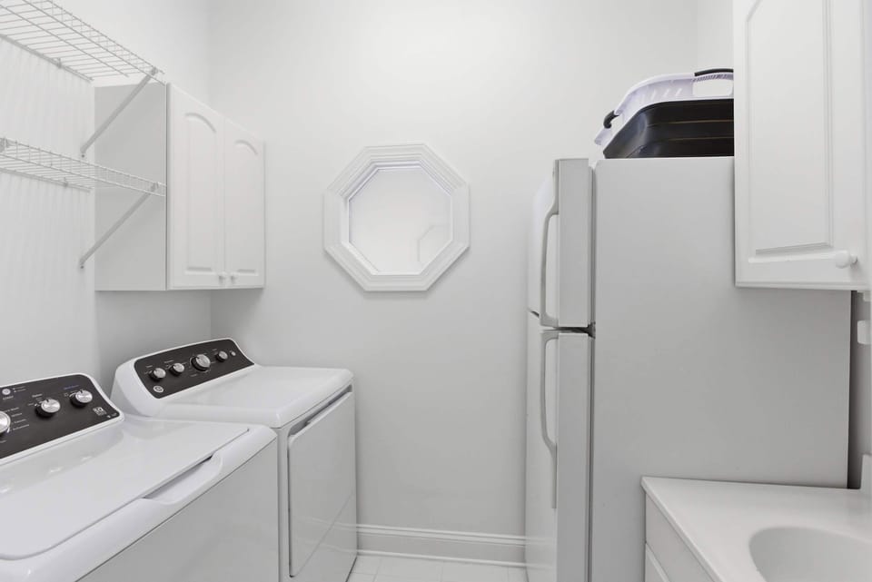 Second-floor laundry room with full-size washer and dryer, extra refrigerator, and abundant white cabinetry.