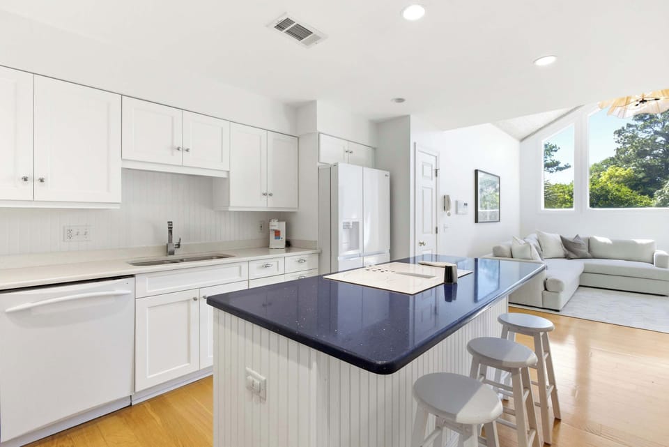 White shaker cabinets, bold navy quartz island, casual bar seating, and an open sightline straight to the living area.