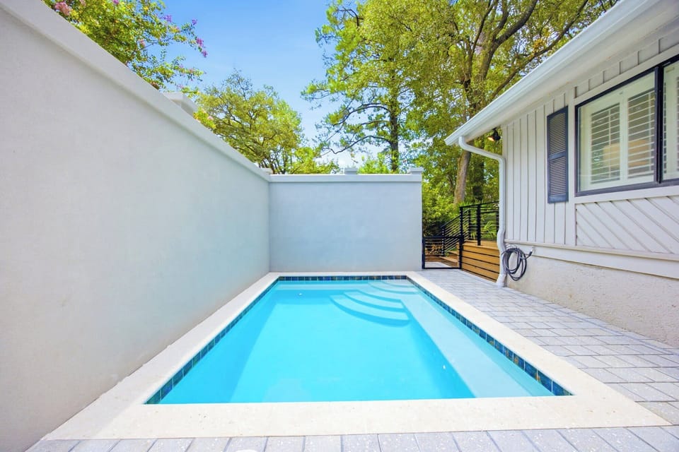 Azure water shimmers in this secluded plunge pool, framed by clean stone lines and tall privacy walls. Lush green trees peek over the edge to provide a quiet, airy backdrop for a refreshing afternoon dip.