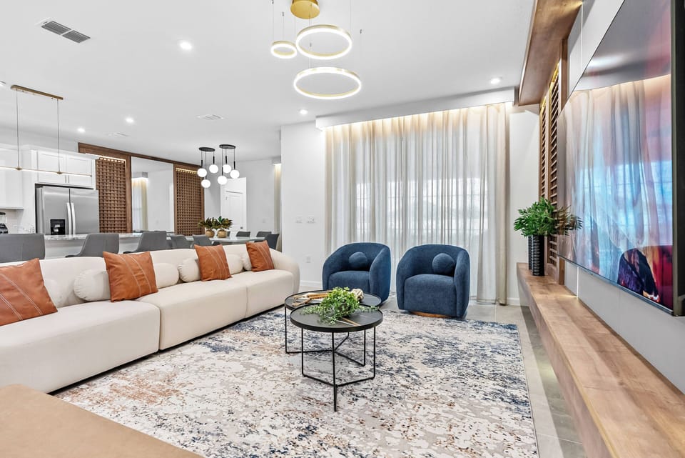 Enjoy a stylish living room with a cozy sectional adorned with earthy-toned pillows and rich blue accent chairs, all bathed in soft lighting that highlights warm wood accents for the ultimate relaxation and conversation space.