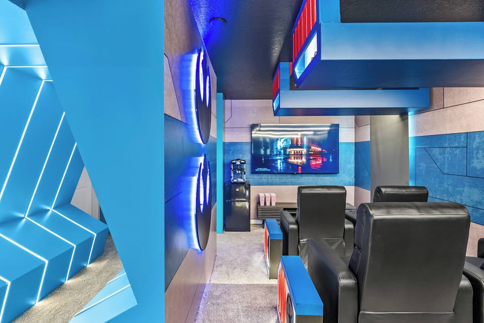 Enter this lively entertainment room, where bold blue walls and sleek black seating set an inviting tone. Enjoy movie nights on the large screen surrounded by unique geometric decor that ignites excitement.