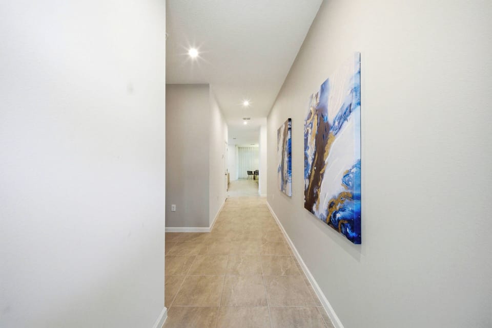 Enter a bright hallway filled with vibrant artwork that livens up the soft, neutral walls. The sleek tile flooring leads you smoothly to the inviting living areas, ensuring a warm and welcoming atmosphere as you explore.