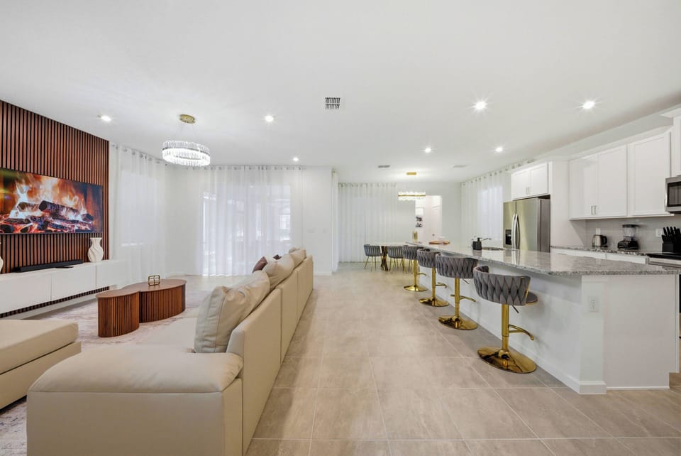 Relax in the bright living area featuring cozy neutral seating and warm wood accents. The stylish kitchen island bar stools are perfect for casual gatherings, while natural light enhances the inviting atmosphere throughout.