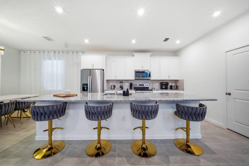 This stylish kitchen boasts a spacious island with elegant gold-accented stools, ideal for casual meals or morning coffee, while bright white cabinetry and modern appliances create an inviting atmosphere for delightful cooking.