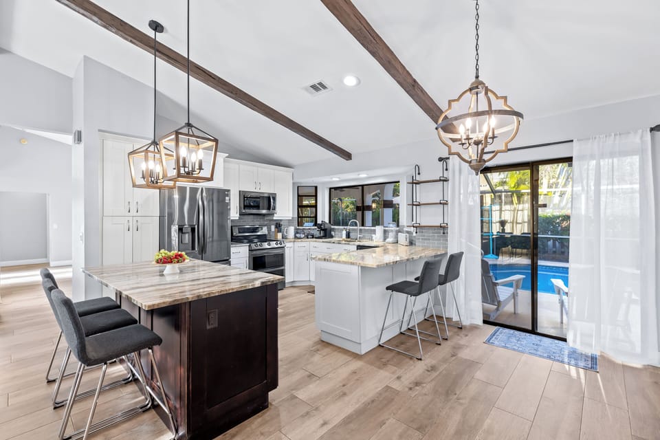 Bright open-concept kitchen with vaulted ceilings, dual islands, and direct access to the screened pool patio.
