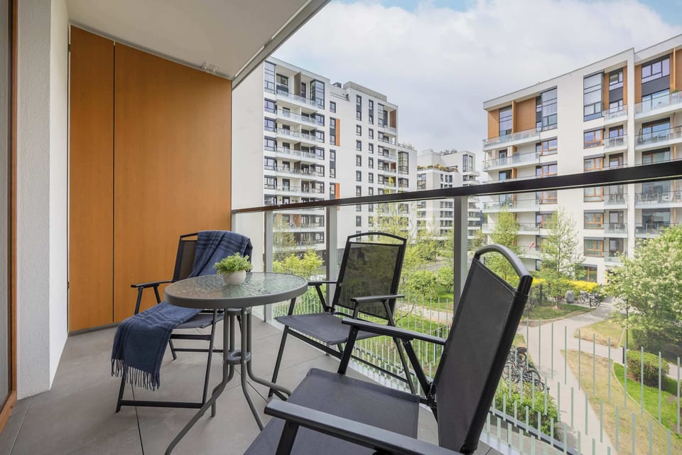 A furnished balcony with black chairs and a small table overlooking modern apartment buildings. The space is perfect for relaxing outdoors.