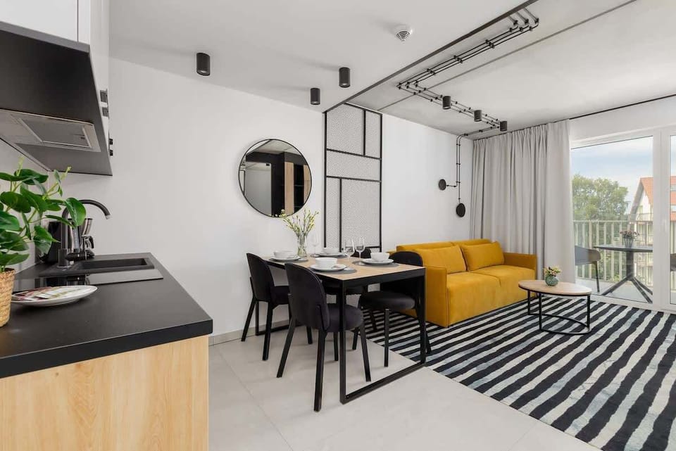 Dining area with a striped rug, black table and chairs, and yellow sofa in the background.


