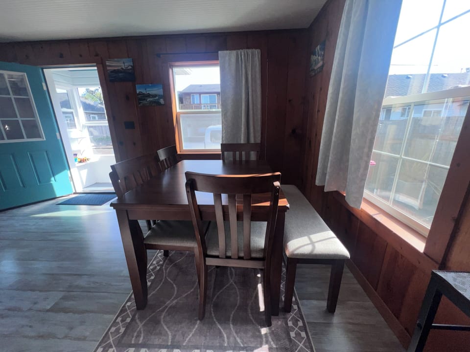 Gather around the wooden dining table where morning coffee and evening meals become cherished memories, with natural light streaming through nearby windows to brighten your stay.