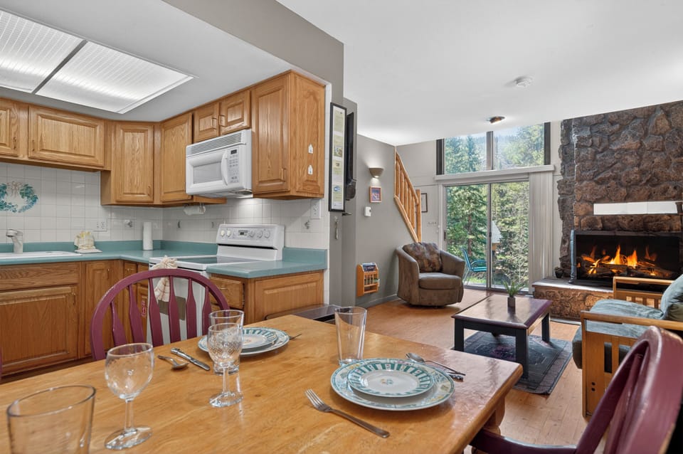 Unwind in your open-concept space where warm wood tones, a cozy stone fireplace, and forest views create the perfect mountain retreat for your gatherings.