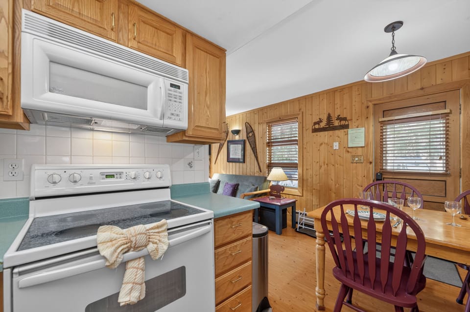 Your cozy cabin kitchen awaits with everything you need: full stove, microwave, and dining space where you can gather around the rustic wooden table after a day of mountain adventures.