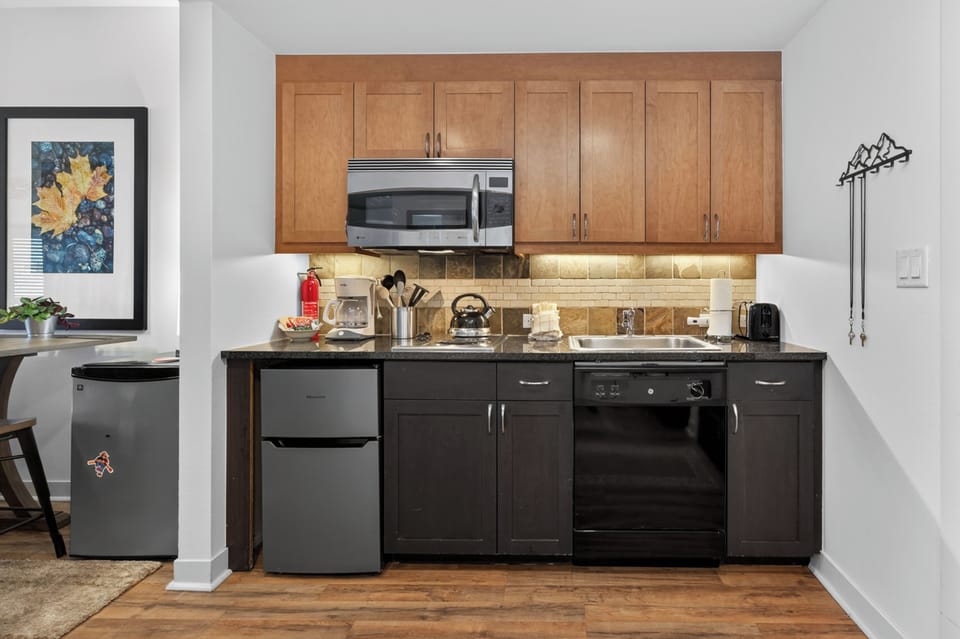 Your compact kitchen features everything you need to whip up meals during your stay, from a full-sized fridge to a microwave, oven, and stove—all complemented by warm wood tones and granite counters for a cozy cooking experience.
