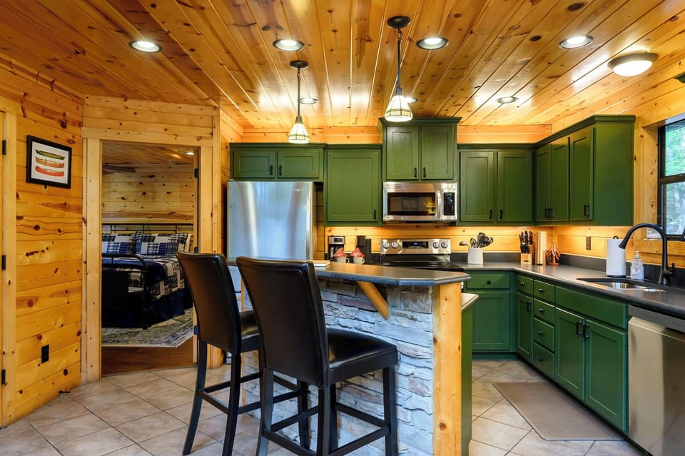 Picture yourself gathering at this rustic kitchen island, bathed in warm cabin light. Forest-green cabinetry and knotty pine surround you, blending mountain charm with modern comforts for memorable meals together.