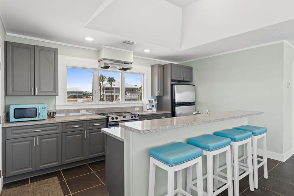 Your bright kitchen features granite counters, modern appliances, and a breakfast bar perfect for casual meals or coffee while enjoying the tropical view through the window.