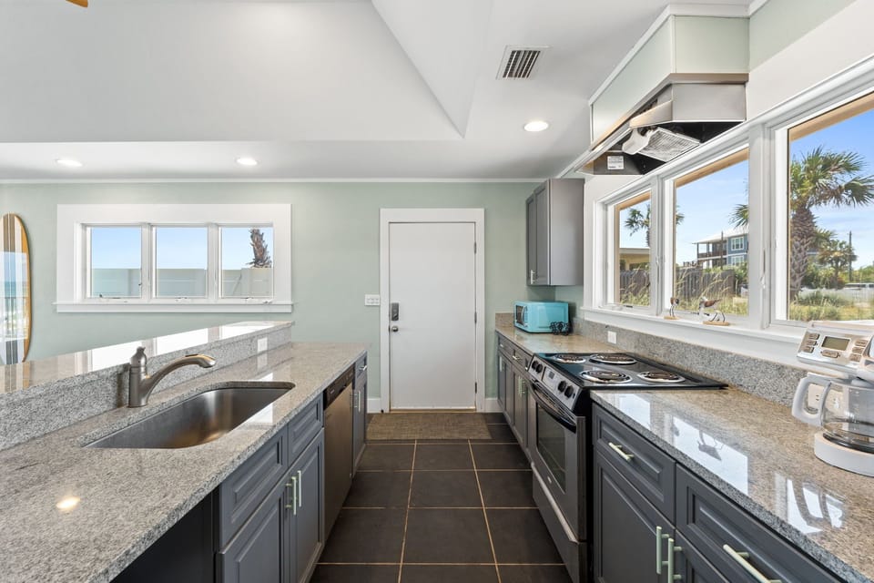 Picture yourself cooking with ocean breezes drifting through windows framing palm trees and coastal views. This bright, modern kitchen features granite countertops, stainless appliances, and ample space for meal prep.