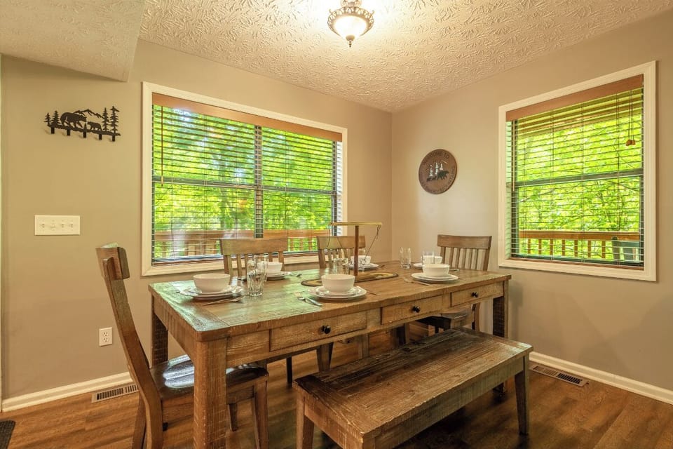 Gather around your rustic dining table for memorable meals with loved ones. Bright windows frame lush greenery, filling your space with natural light and peaceful woodland views as you dine.