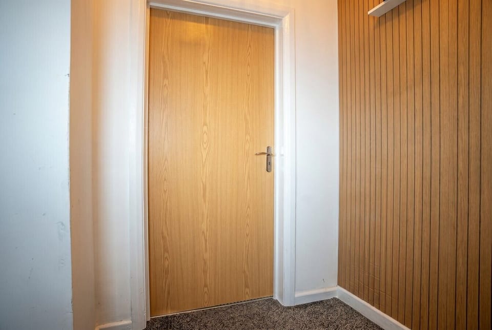 Wooden interior door beside a slatted feature wall and carpeted floor.