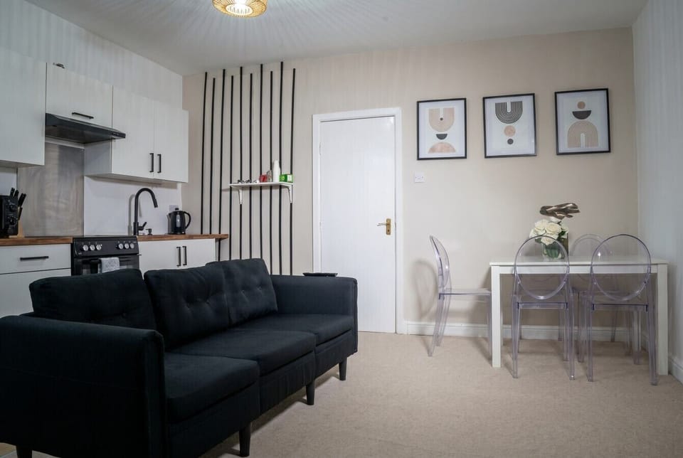 Open-plan living and dining area with a sofa, table with chairs, and a kitchenette with sink and kettle.