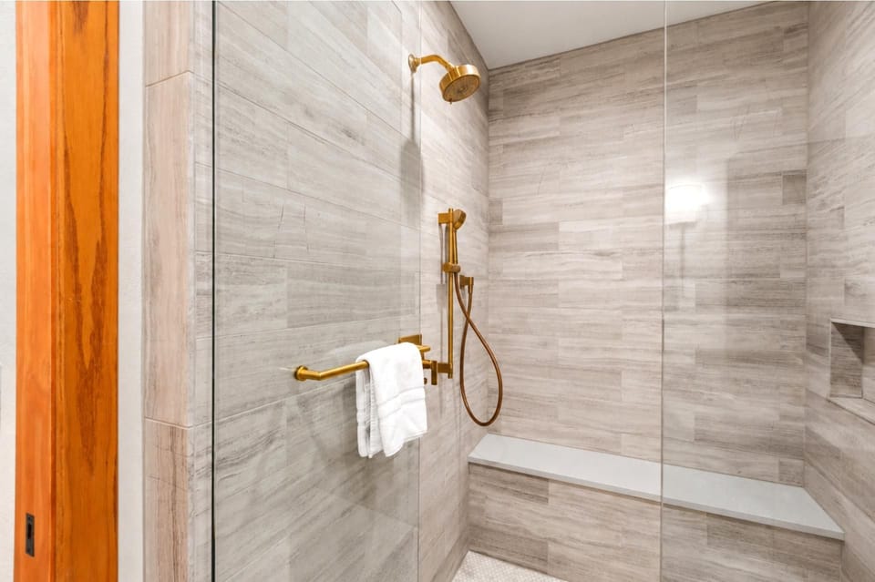 Spa-inspired shower with sleek tile, built-in bench, and gold fixtures for a luxurious touch.