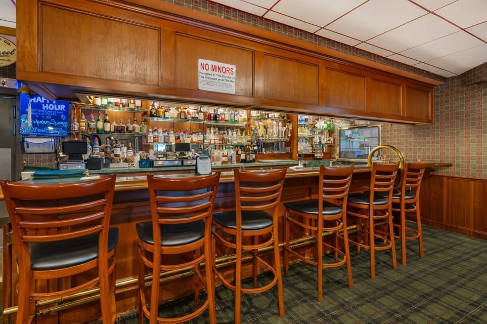 Full bar with wood-panelled cabinetry, green marble countertop, bar stools, draft taps, and a full back-bar of spirits — happy hour runs daily.