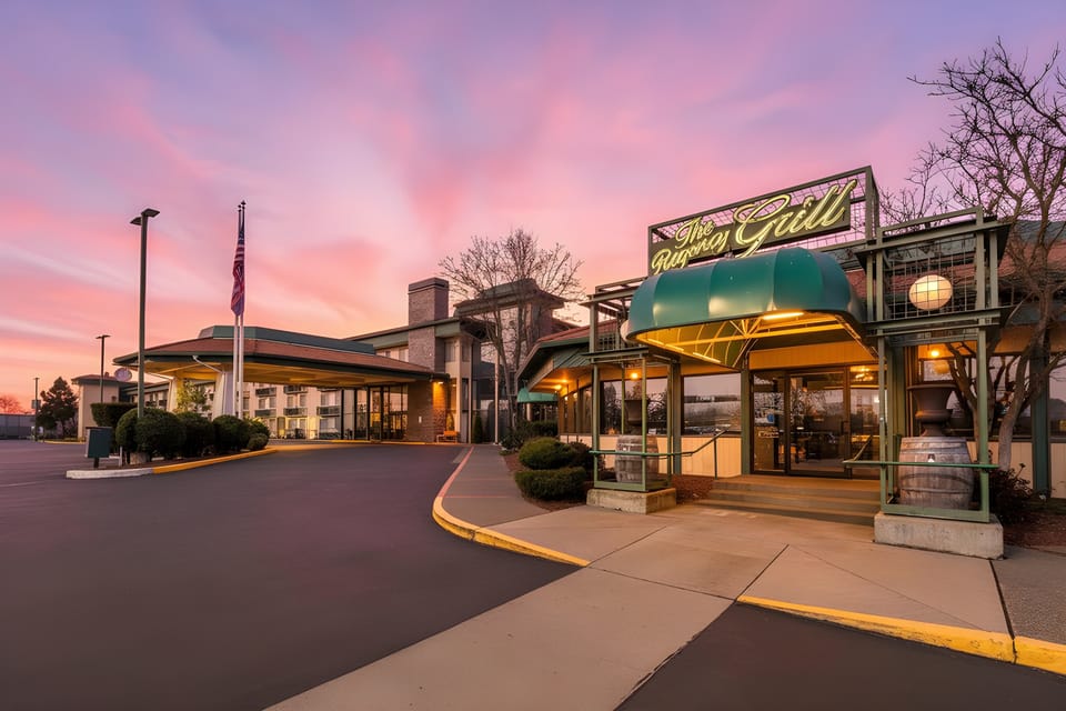 Hotel exterior and restaurant entrance at dusk, with the on-site grill and green awning lit up under a pink evening sky.