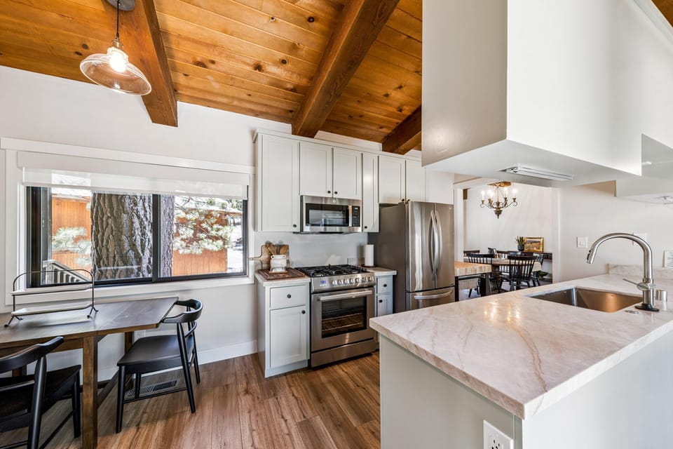 Marble countertops and stainless steel appliances complement white cabinetry beneath exposed wood ceiling beams.