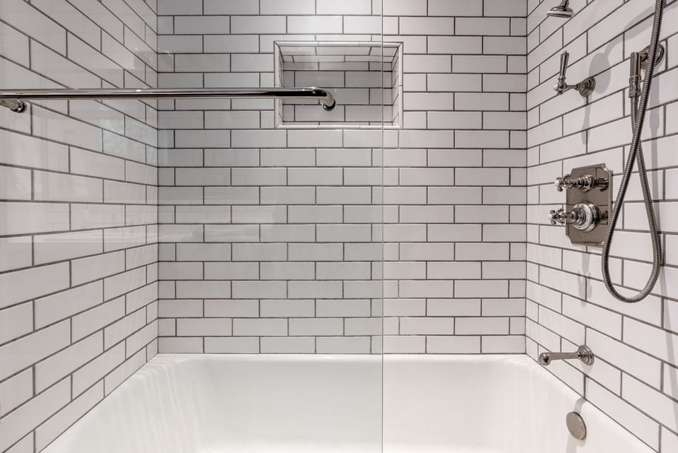 Bathtub and shower combination featuring white subway tile and chrome fixtures.