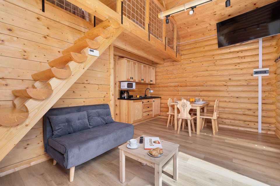 A modern sofa in the lounge area is positioned under the stairs, creating a comfortable TV nook. A large TV is mounted above the cabinet, perfect for movie nights.