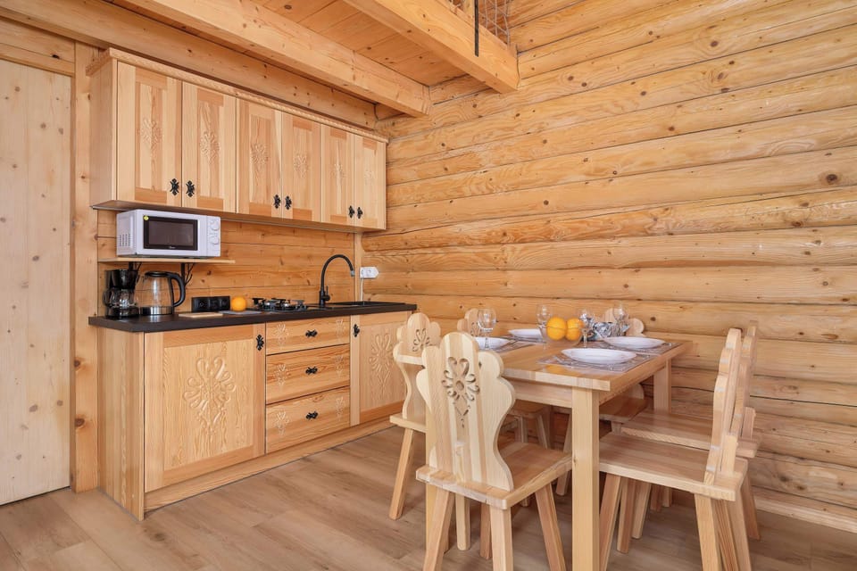 A compact kitchenette equipped with essential appliances and a wooden dining table with carved chairs. The functional built-in cabinets harmoniously complement the raw style of the wooden walls.