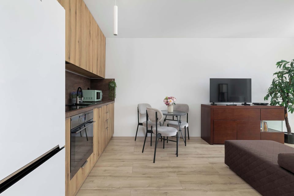 The kitchenette is shown from the living room, emphasizing the open and social layout of the apartment. A round dining table connects the two functional zones.