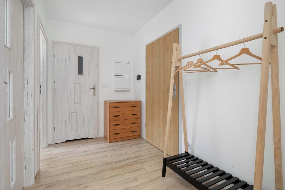 An entrance area features a practical wooden coat rack and a matching shoe cabinet. The white front door and bright walls create a clean first impression.
