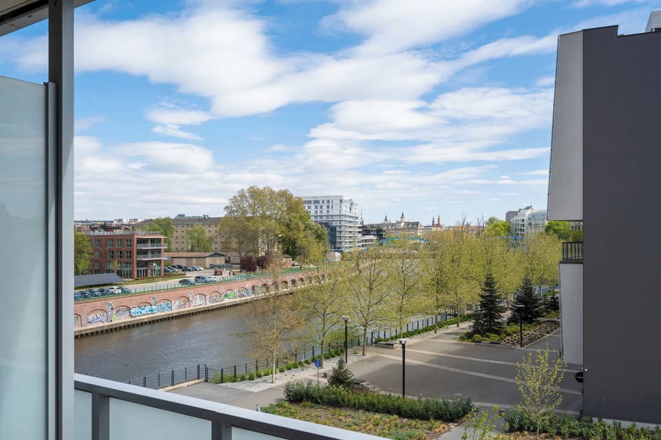 A panoramic view from the balcony overlooking a park, the canal, and the surrounding urban landscape.