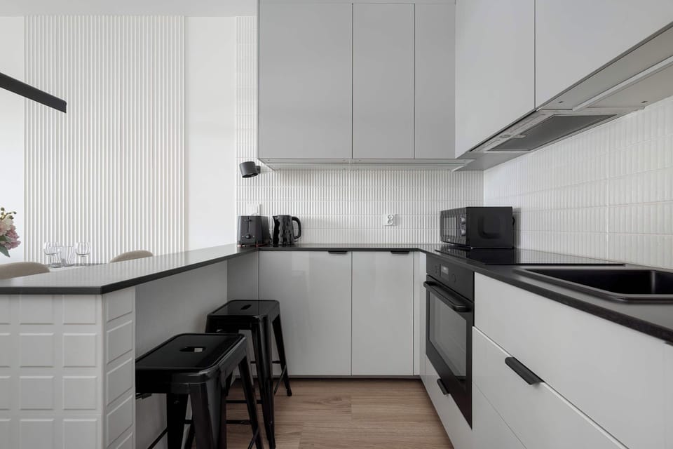 A compact, U-shaped kitchenette with white cabinetry, a black counter, integrated appliances, and a tiled backsplash.