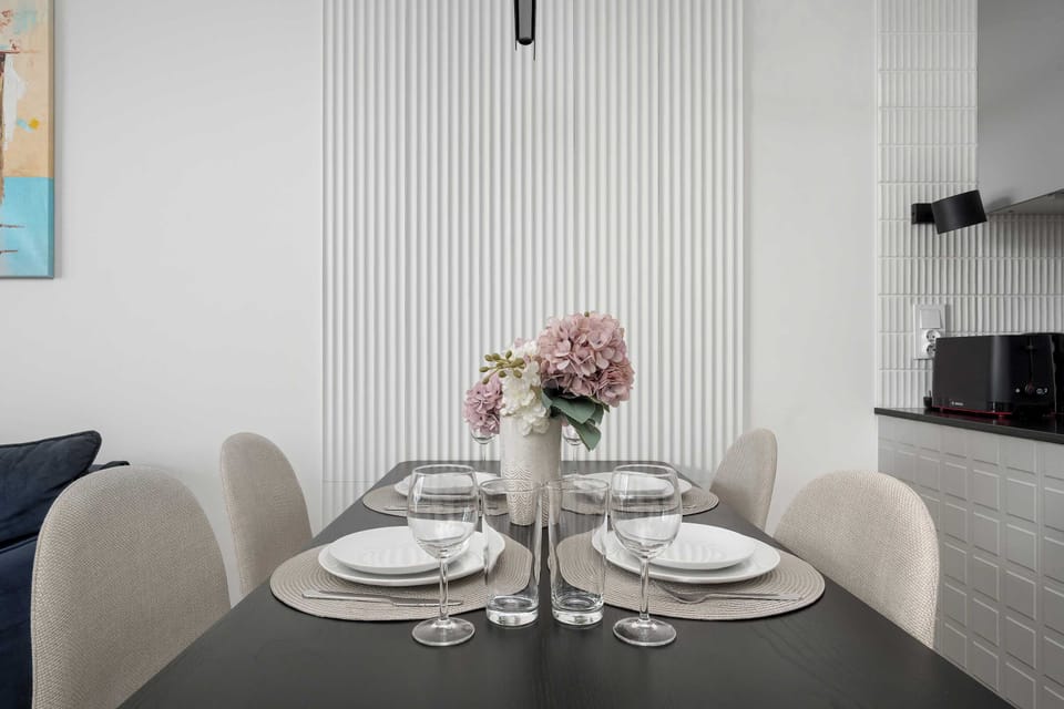 Close-up of a modern dining table neatly set with plates, cutlery, a flower vase, and upholstered chairs.