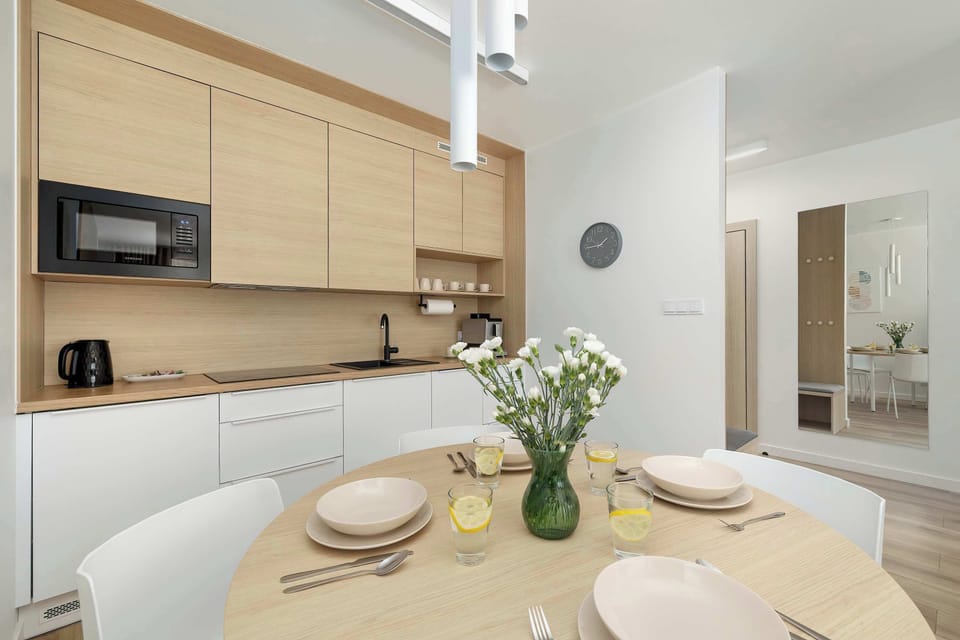 Sleek and functional kitchenette featuring light wood cabinetry, integrated appliances, and a minimalist dining area. Designed for modern living.