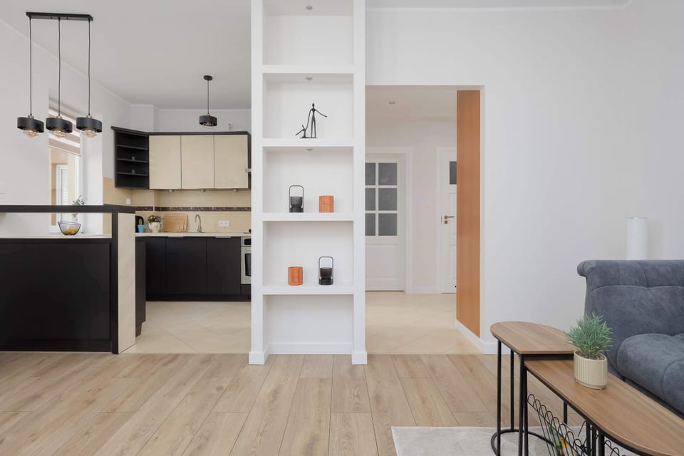 A view from the living room toward the kitchenette, separated from the living area by a white, open-shelf bookcase.