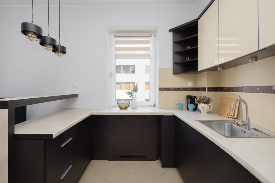 A modern kitchenette with dark lower cabinets and light-colored upper cabinet fronts, illuminated by stylish pendant lights.