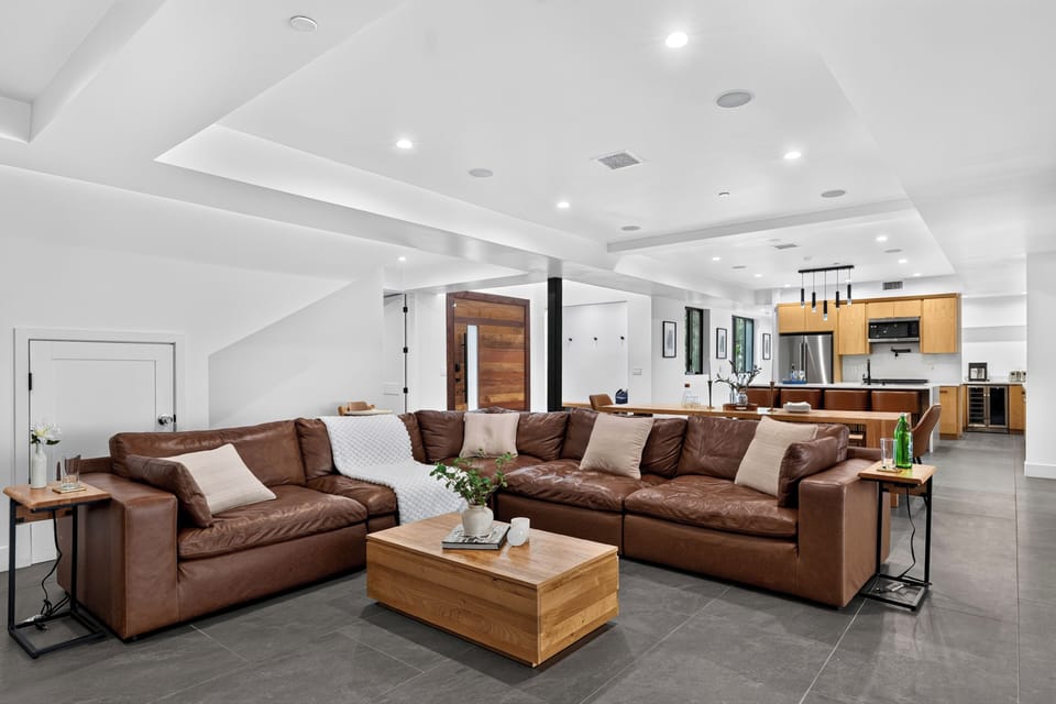Modern living room with a leather sectional, dramatic stone fireplace wall, and seamless flow to the covered outdoor lounge.