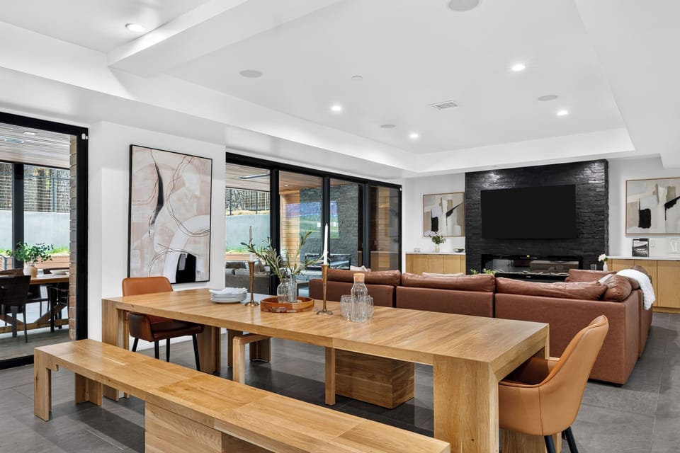 Open dining and living area with warm wood accents, leather seating, and seamless access to the covered outdoor lounge.