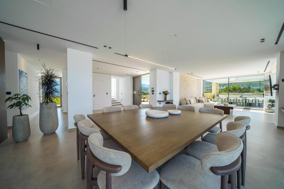 At the heart of the space, a grand dining table comfortably seats up to 12 guests, set against a captivating backdrop of the blue sky and sea