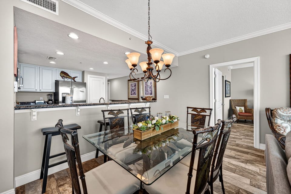 Picture yourself gathering around this elegant glass dining table, bathed in warm chandelier light.