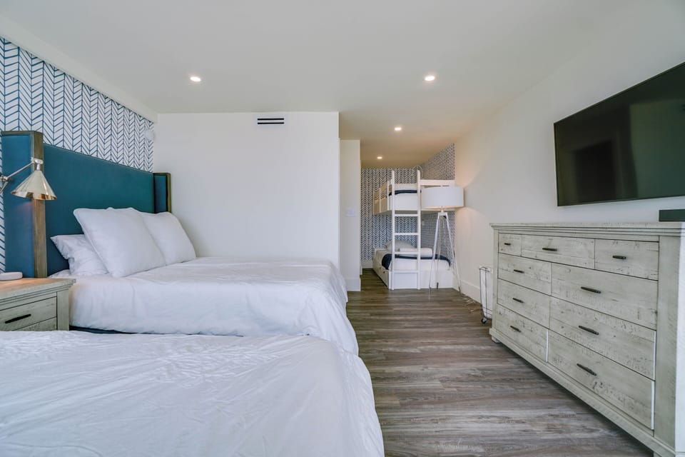 Your spacious family suite features plush beds with crisp white linens, stylish coastal decor, and a clever bunk nook—perfect for kids or extra guests seeking their own cozy corner.