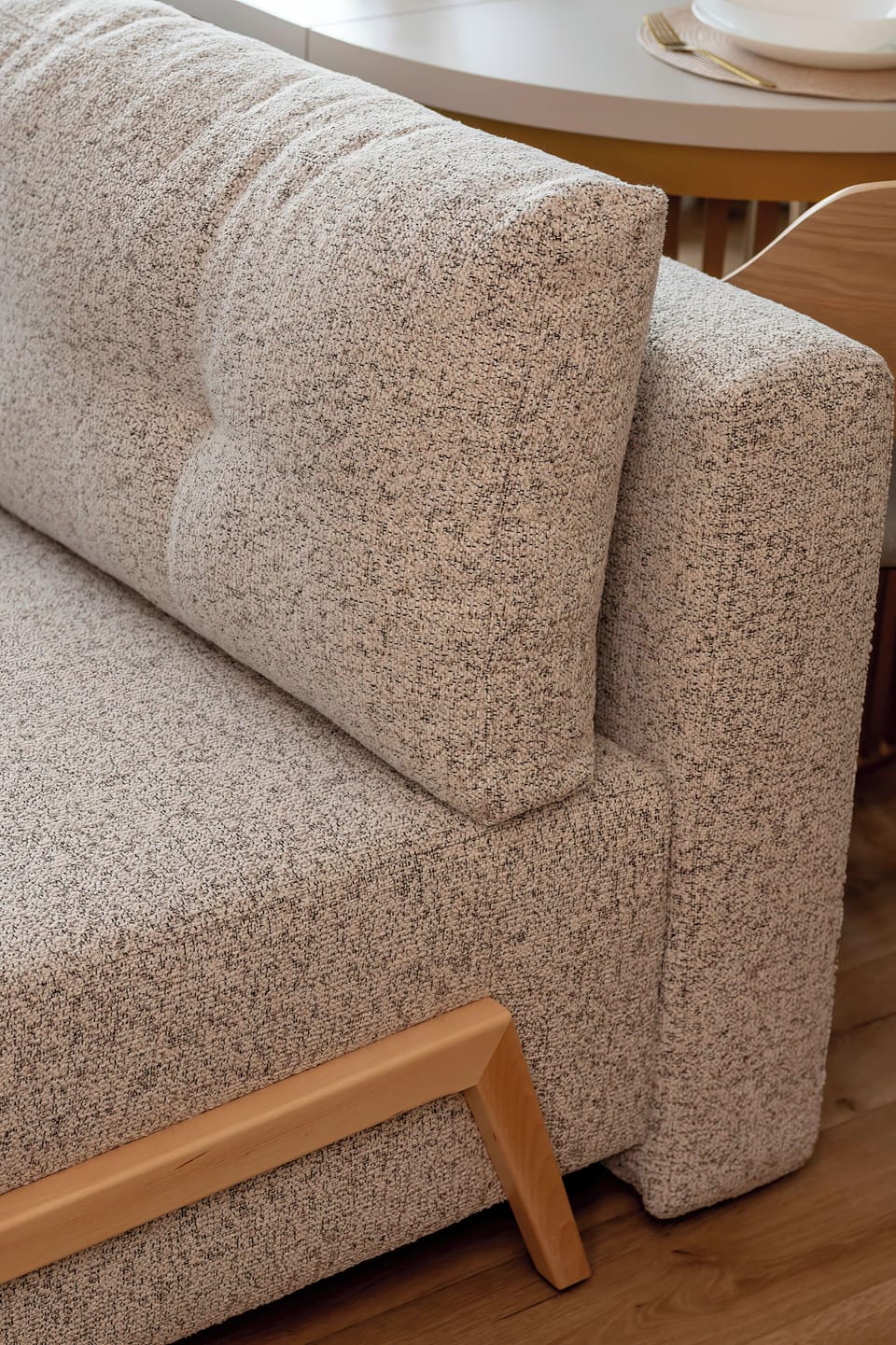 A close-up of furniture highlights the textured, speckled fabric of the sofa cushion. The light-toned wooden legs of the furniture emphasize the Scandinavian-inspired design.