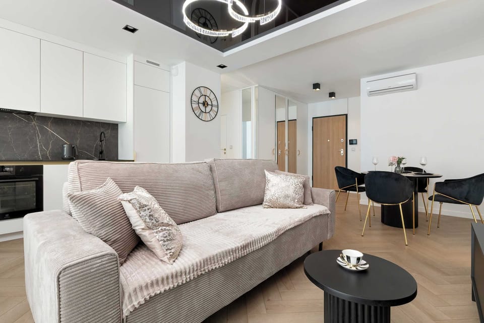 The living room opens up to a dining area with a dark table and chairs. A white sofa provides a comfortable seating area under a modern, multi-ring ceiling light.