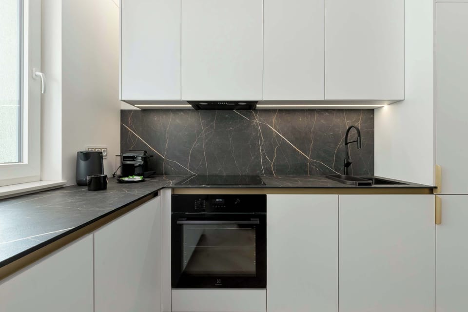 The kitchen features dark backsplash tiling that provides a stark contrast to the white upper and lower cabinets. Built-in appliances, including an oven, are integrated seamlessly into the design.
