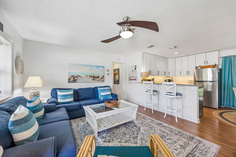 Relax in your bright, coastal-inspired living space with comfortable seating, ceiling fan, and a fully-equipped kitchen ready for your vacation meals.